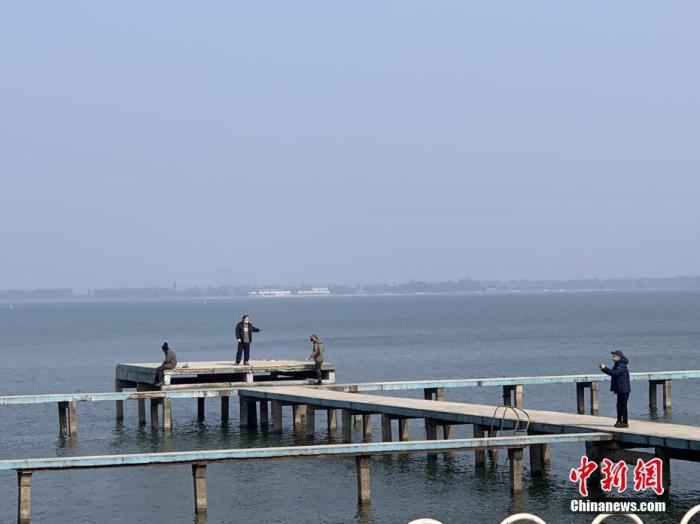1月29日，武汉“封城”第七天，天气放晴，一些市民来到位于武汉大学凌波门外的东湖栈桥上，佩戴口罩晒太阳。 /p中新社记者 杨程晨 摄